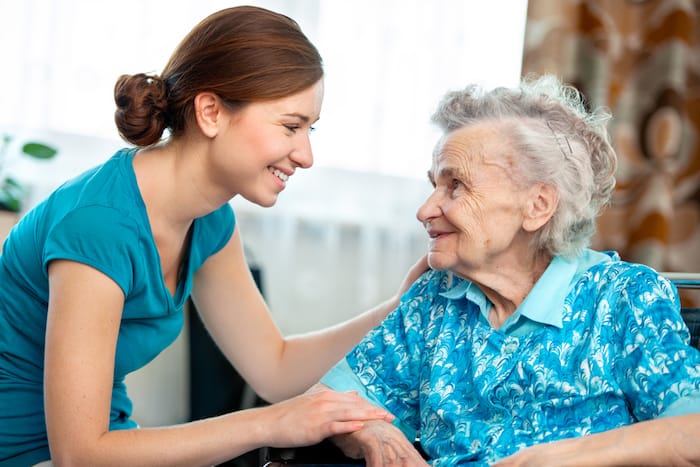 An elderly woman smiles at a younger woman during a post-acute care visit.