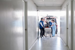 A group of healthcare workers push a patient in a stretcher through a hospital's entrance.